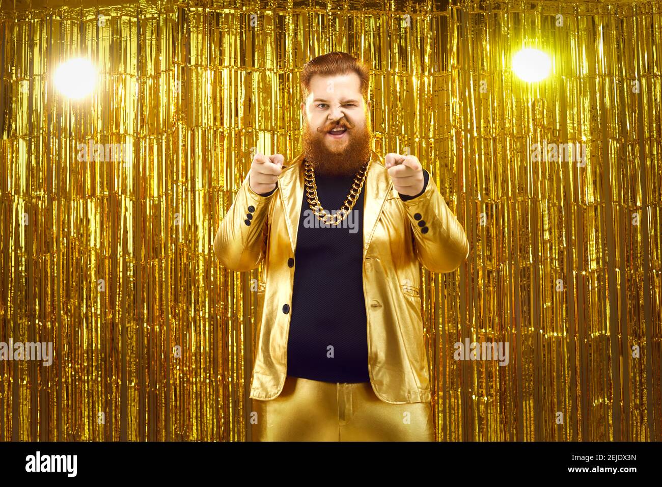 Man in funky golden suit standing against glittering background and pointing at camera Stock Photo