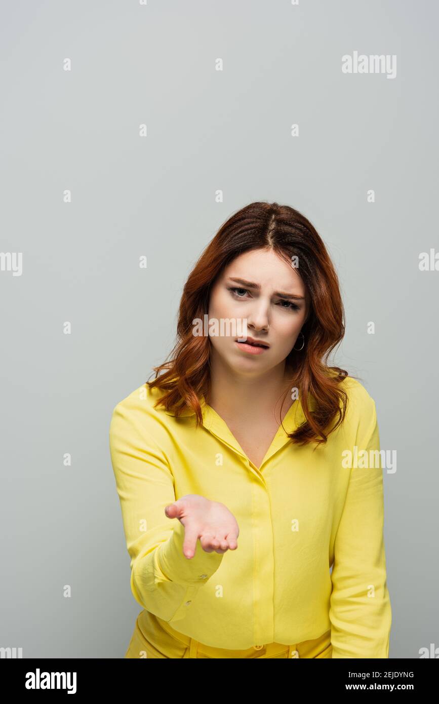 upset woman with curly hair pointing with hand while looking at camera on grey Stock Photo