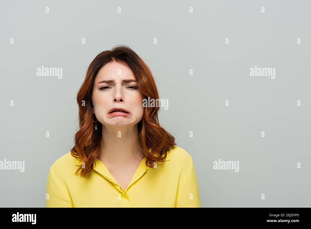 discouraged woman looking at camera and grimacing isolated on grey Stock Photo