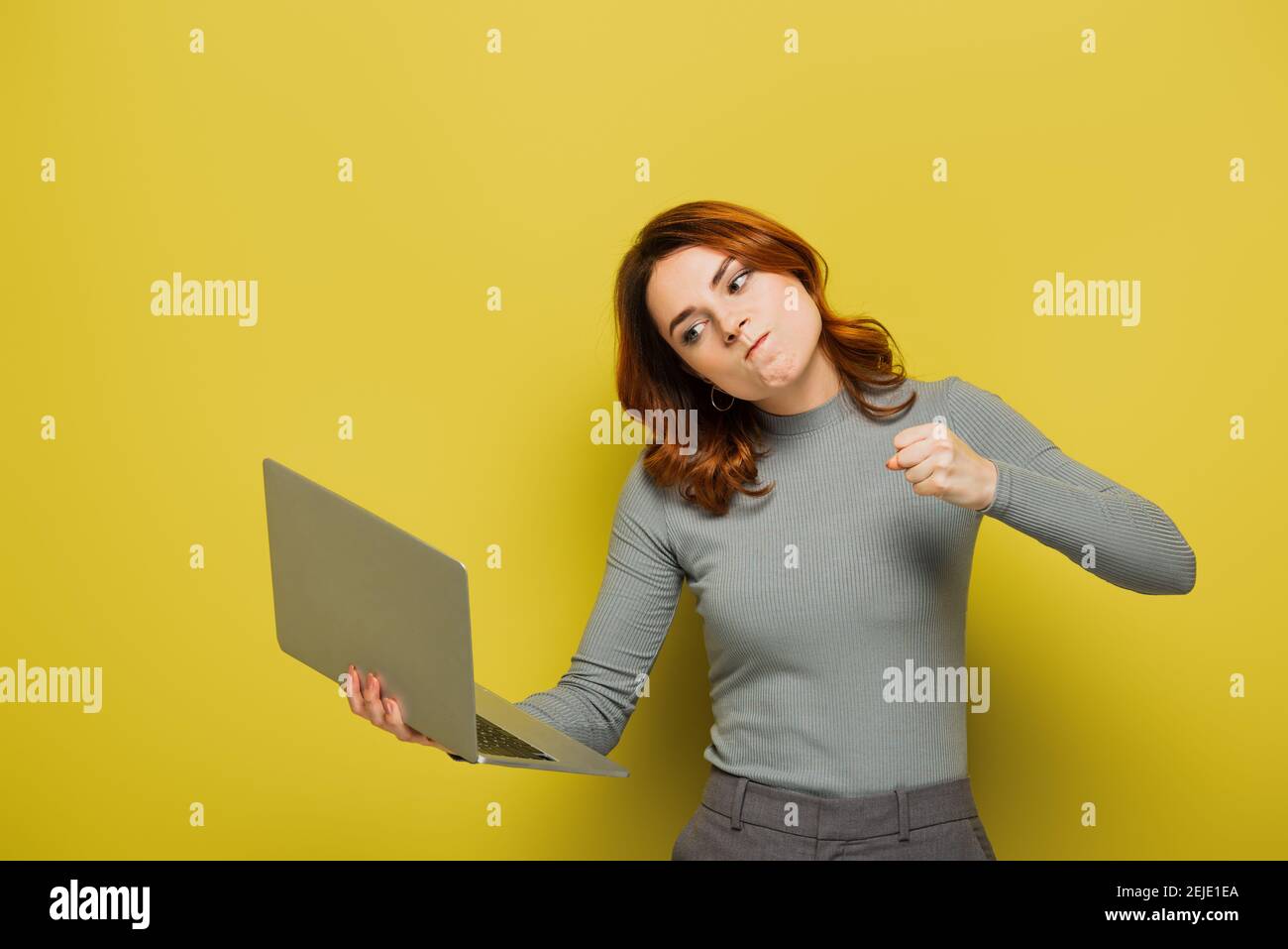 mad young woman with curly hair holding laptop and showing clenched