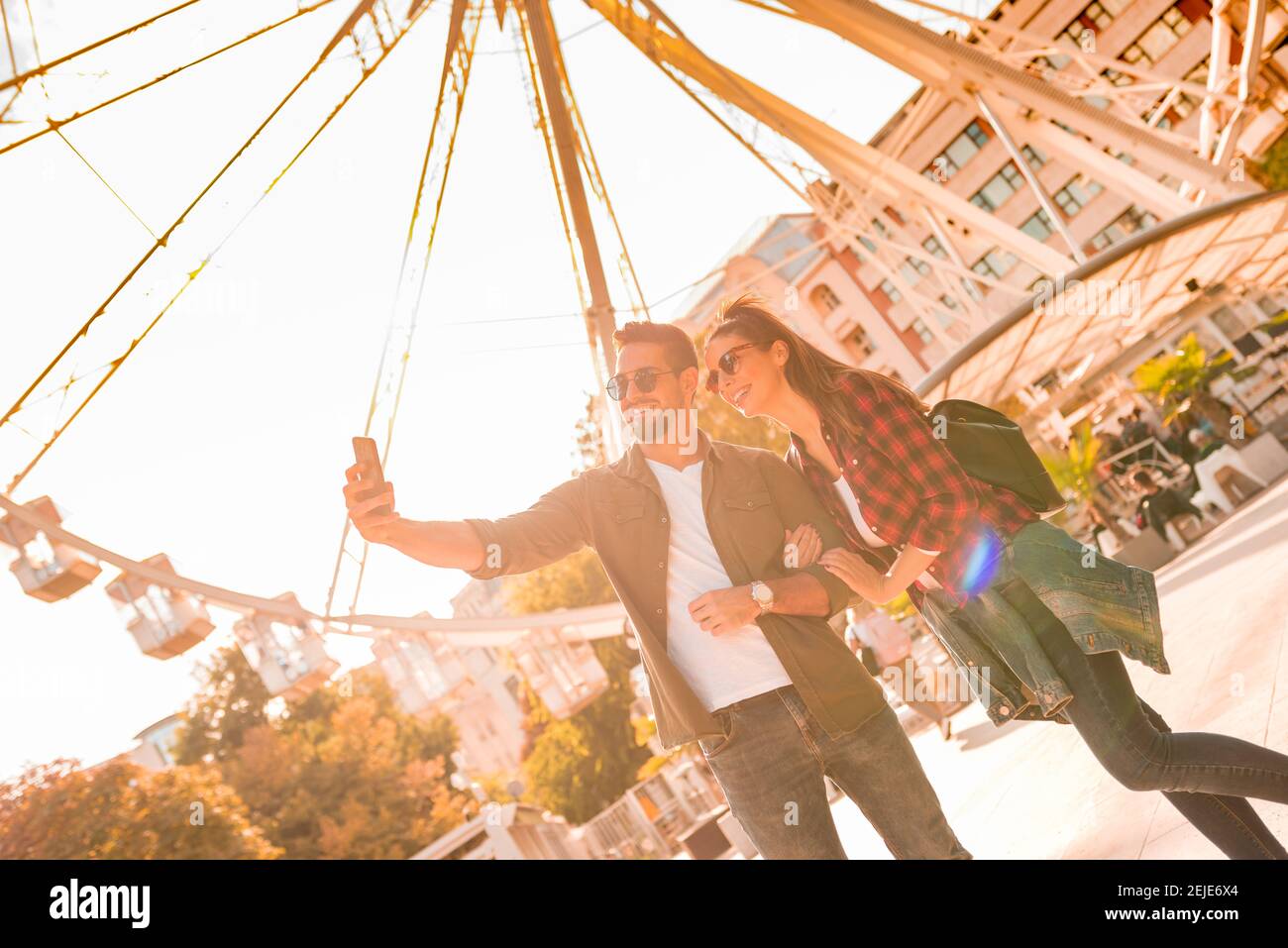 A traveling couple taking a selfie at a Ferris wheel on a sunny summer day. Stock Photo