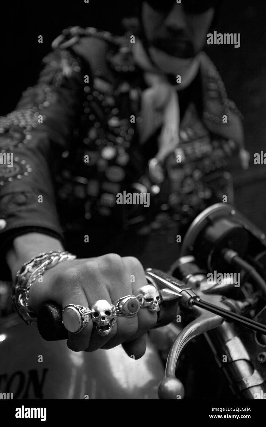 A man wearing leathers hold on to a motorcycle handle, showing off his rings. A man showing scull rings on his clenched fist.Hands close up. Stock Photo