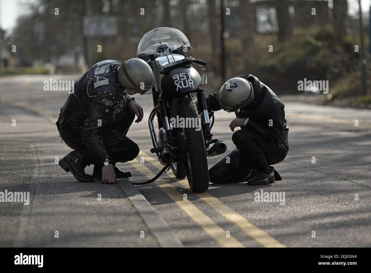 Two men in leather biker gear checking motorbike on road Stock Photo