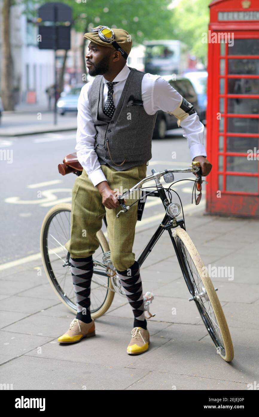 Full length portrait of handsome african man wearing plus fours standing beside bicycle in London Stock Photo