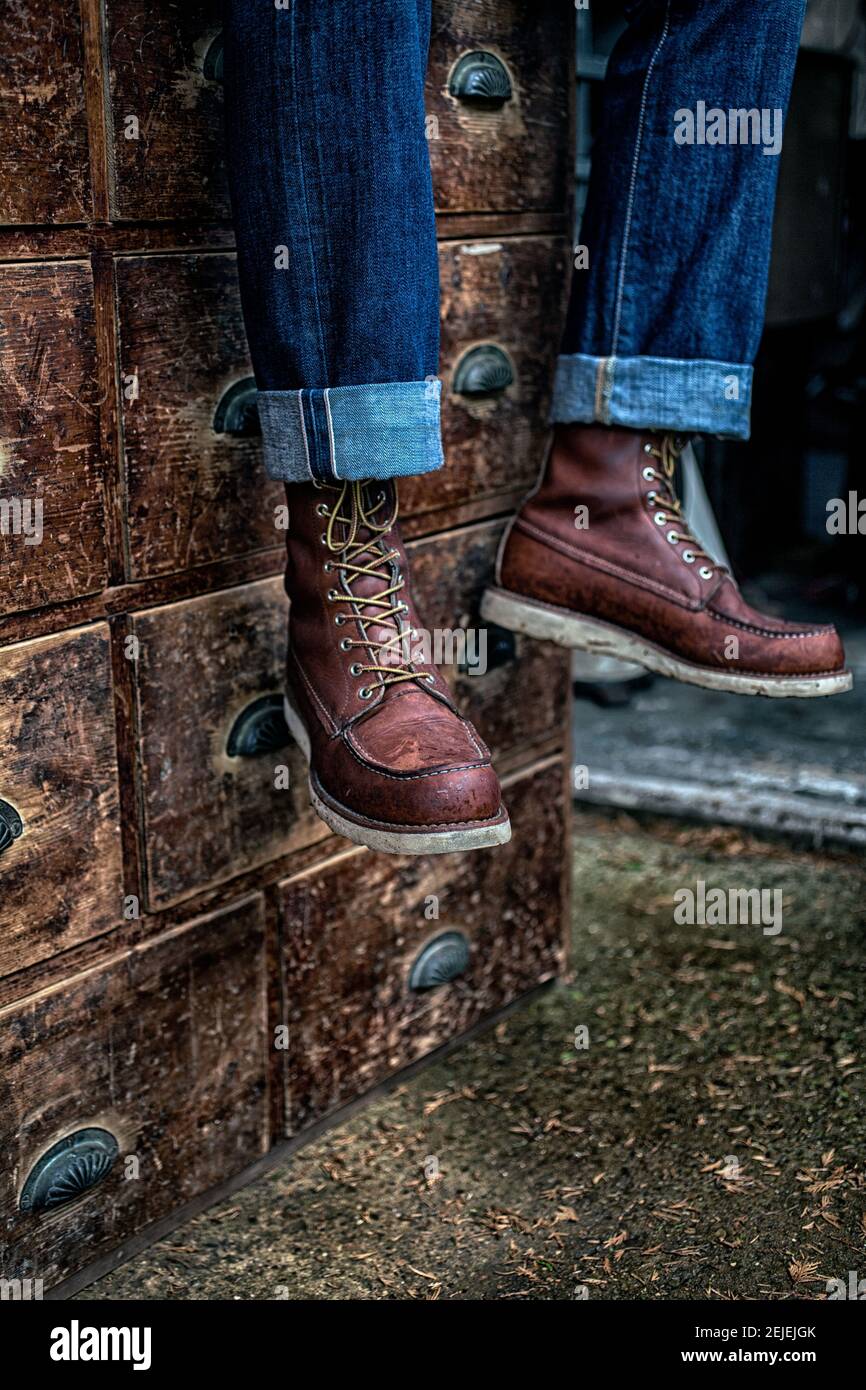 man wearing denim jeans and work boots sitting on antique wooden drawer Stock Photo