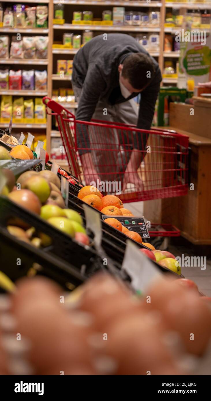 A man with a shopping trolley behind a  fruit stand in a organic grocery store. Plastic free unpacked fruits and vegetables on display. Stock Photo
