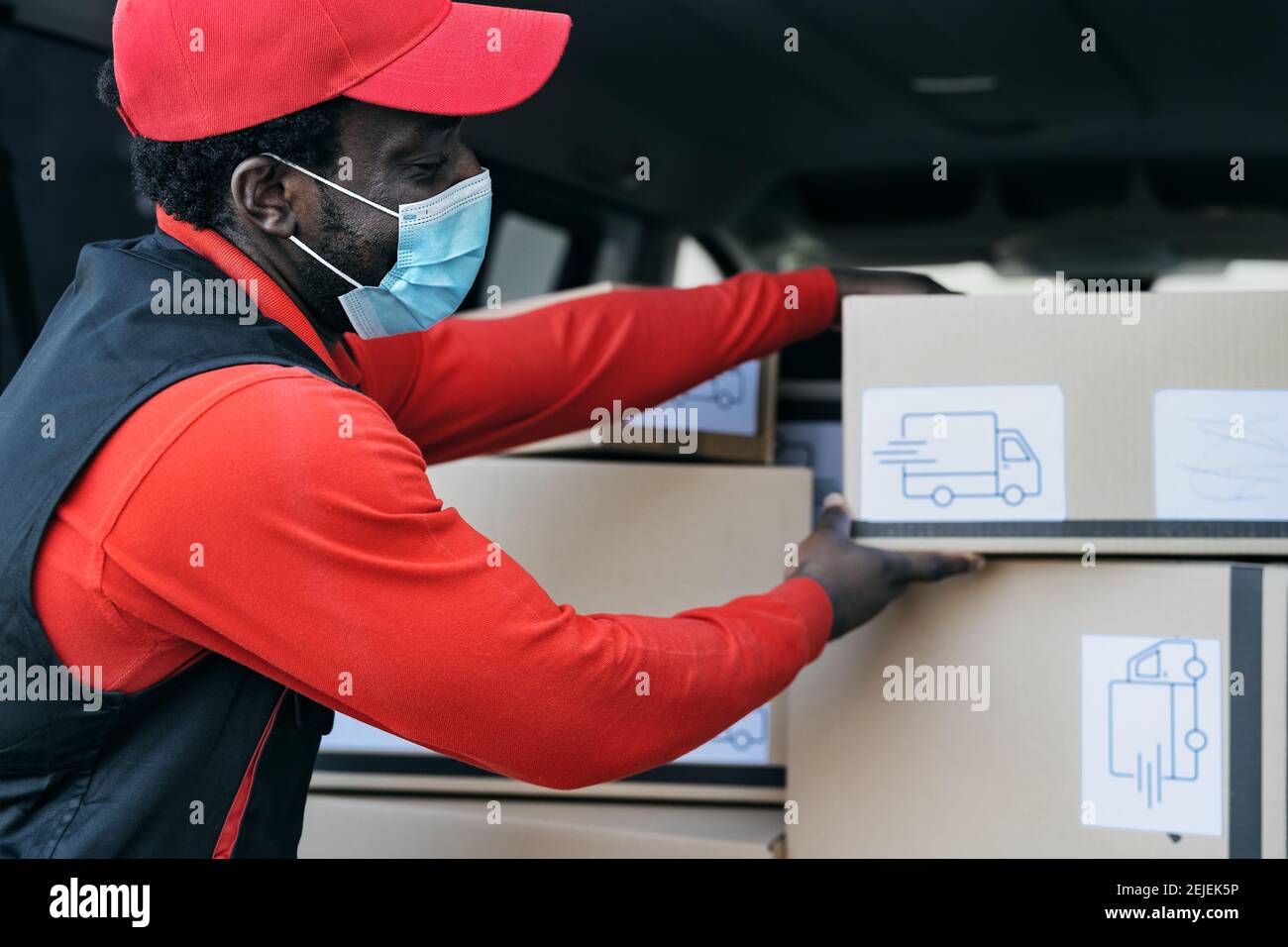 African delivery man loading boxes in the truck while wearing face mask to avoid corona virus spread - People working with fast deliver Stock Photo