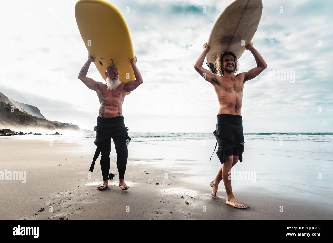 Happy friends surfing together on tropical ocean - Sporty people having fun during vacation surf day - Extreme sport lifestyle concept Stock Photo