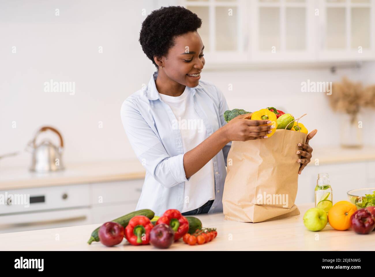 Black Lady Unpacking Grocery Bag After Shopping Standing In Kitchen Stock Photo