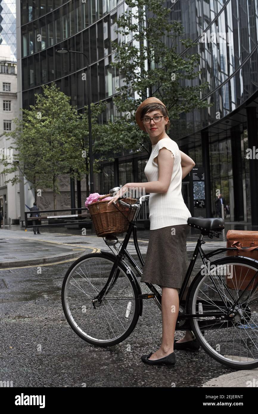 Young woman with bicycle standing outside office building in City of London . Stock Photo