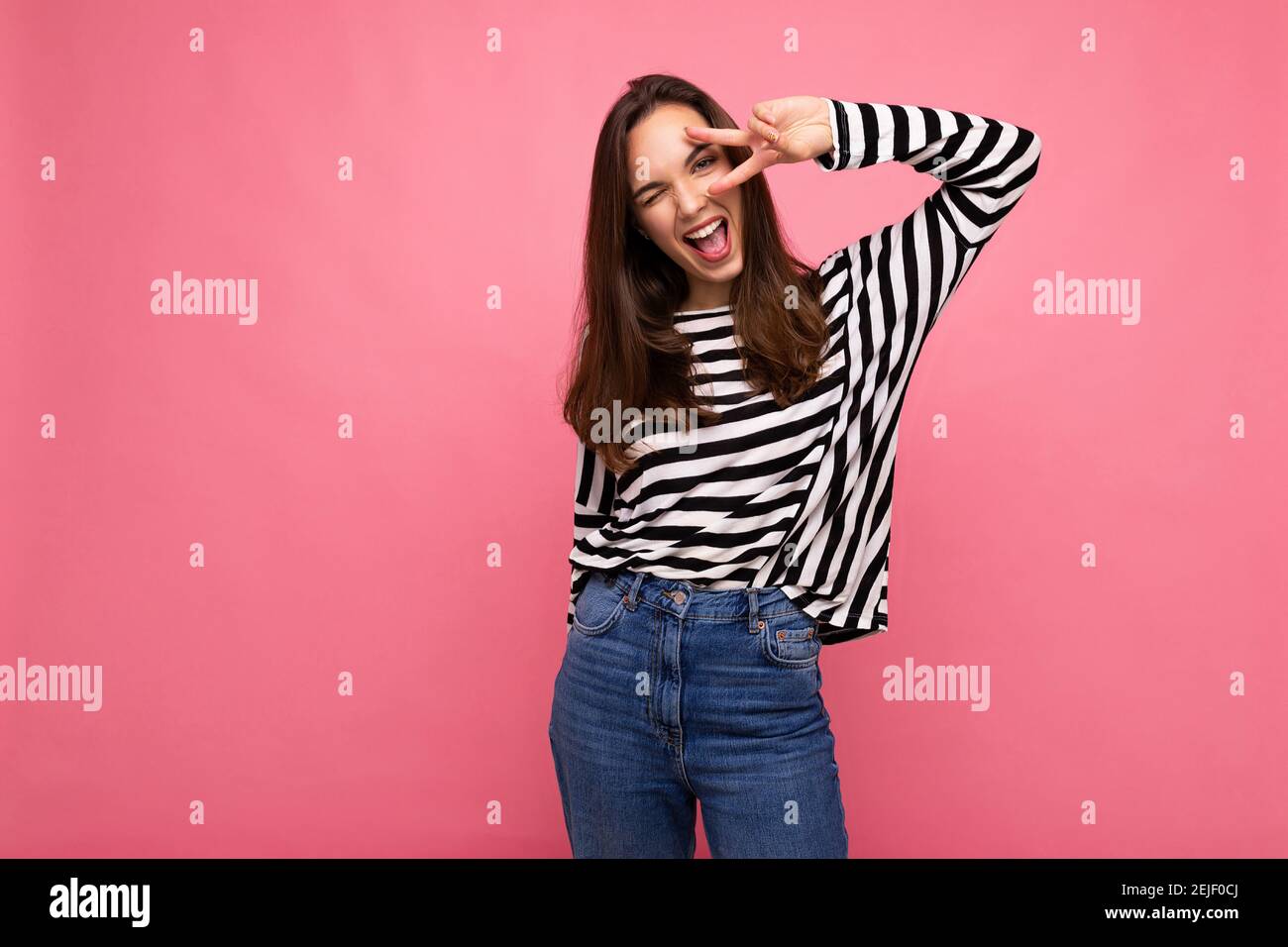 Young positive winsome happy beautiful brunette woman with sincere emotions wearing casual striped pullover isolated on pink background with copy Stock Photo