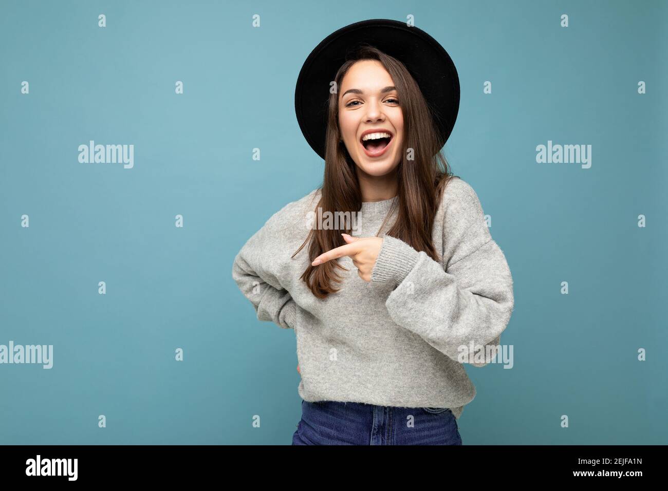 Photo of beautiful brunette happy joyful young woman directing finger to the side with copy space, demonstrating and presenting low prices poster Stock Photo