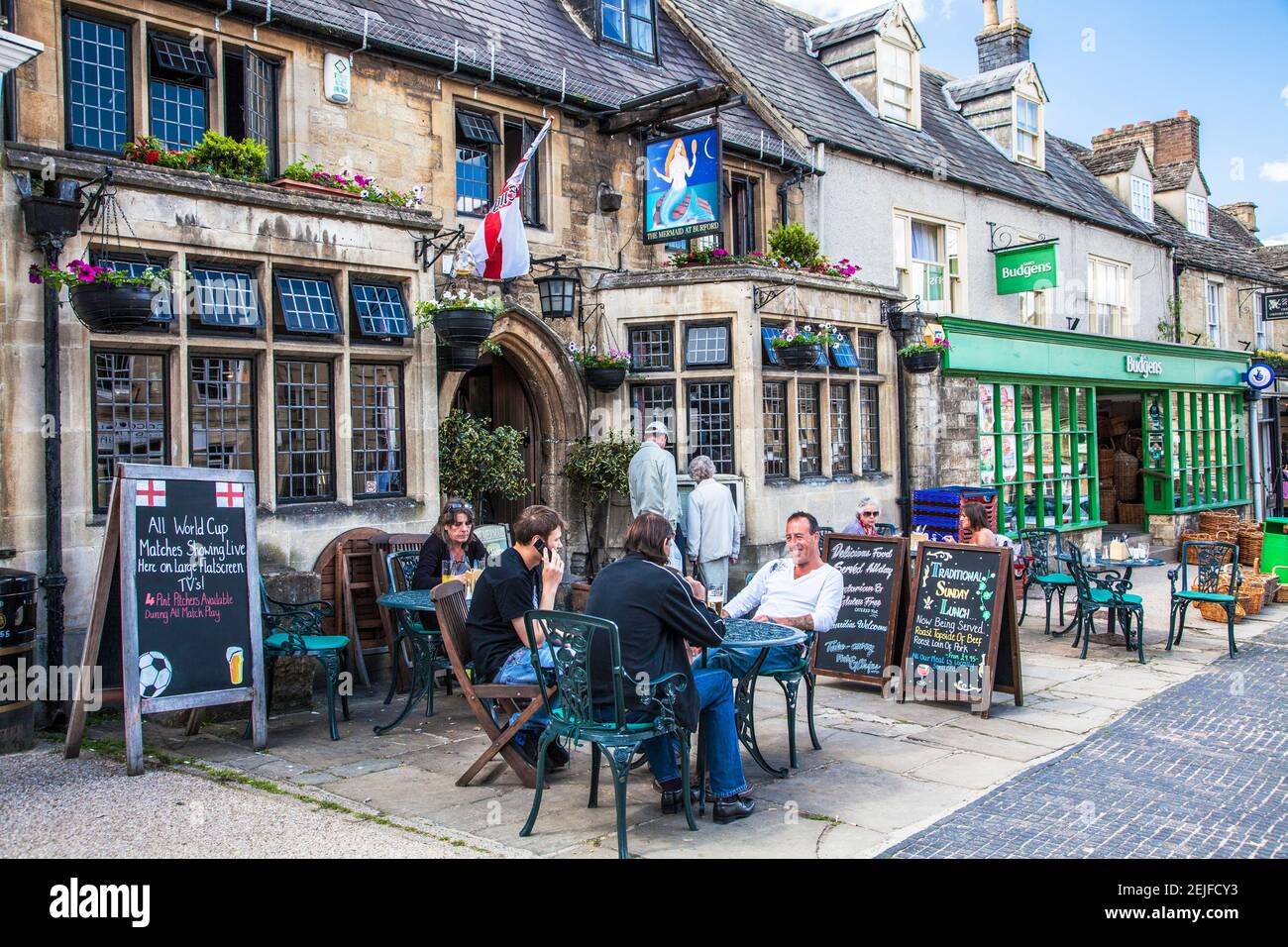 Visitors enjoy a drink outside a pub in the Cotswold village of Burford in Oxfordshire. Stock Photo