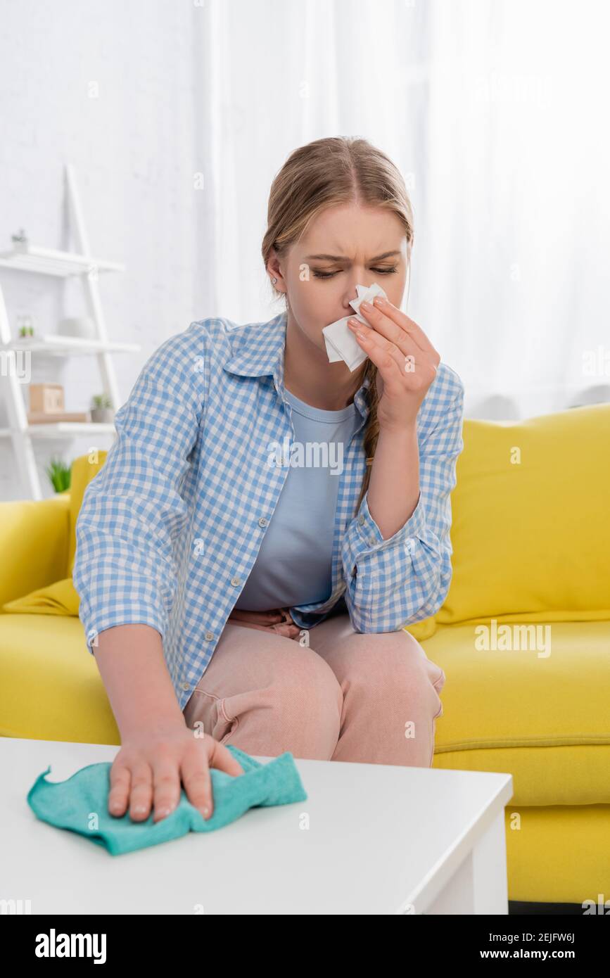 Woman with allergy having snuffle while cleaning table on blurred ...