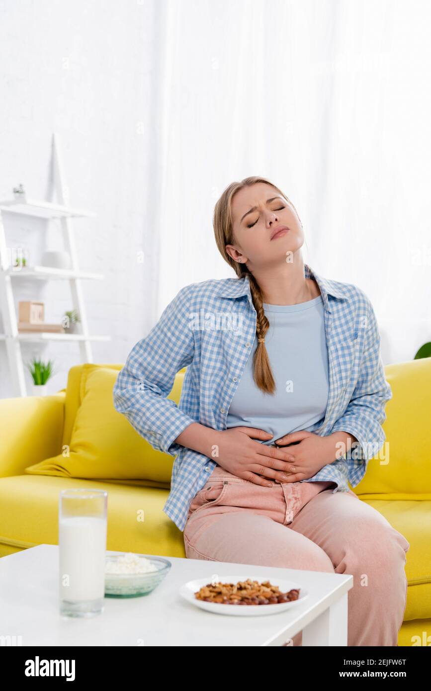 Tired woman with allergy sitting near cottage cheese, milk and nuts on