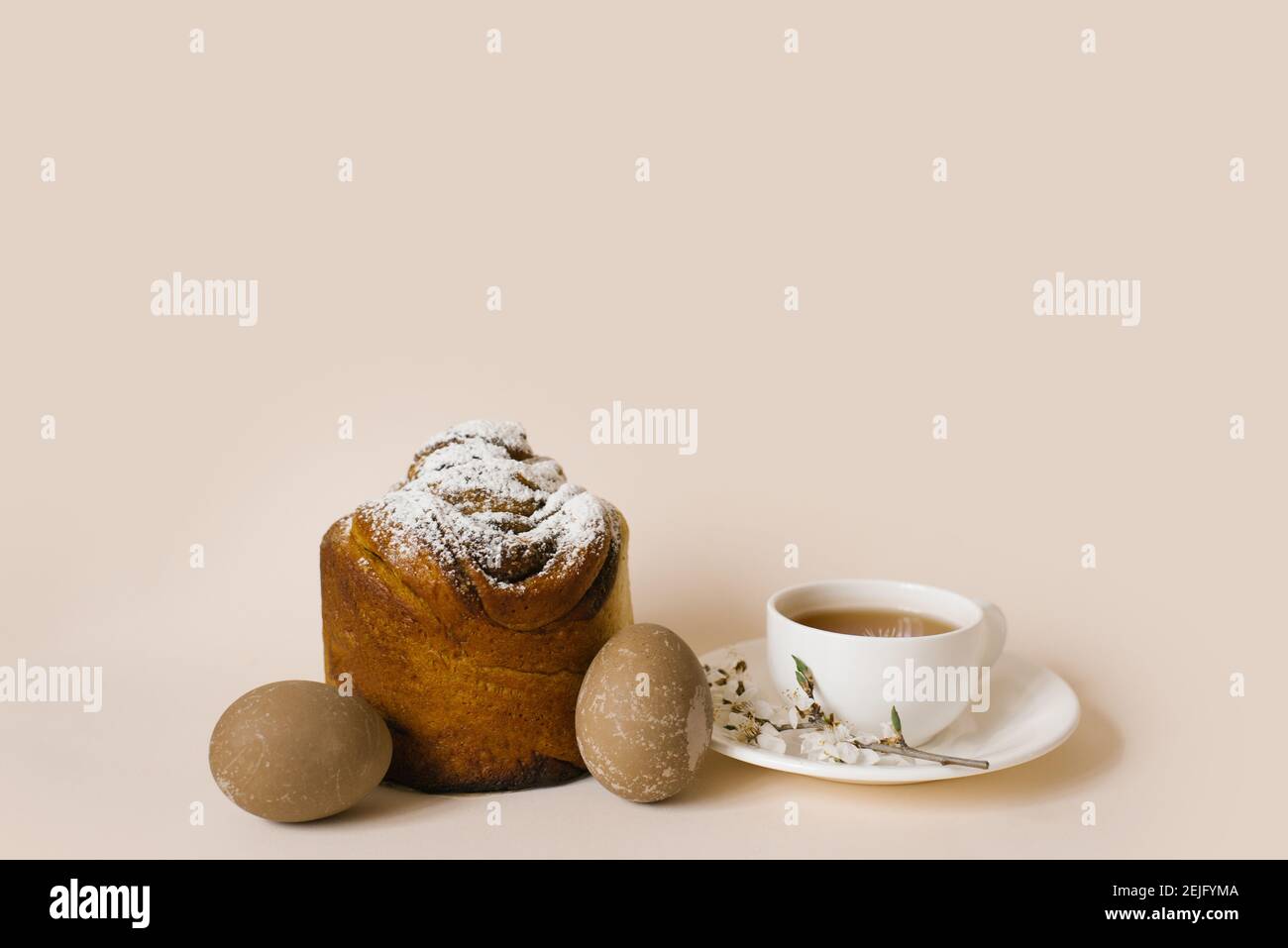 A traditional Easter cake sprinkled with powdered sugar, colored beige eggs and a cup of black tea in a white mug and a sprig of apple blossom. Holida Stock Photo