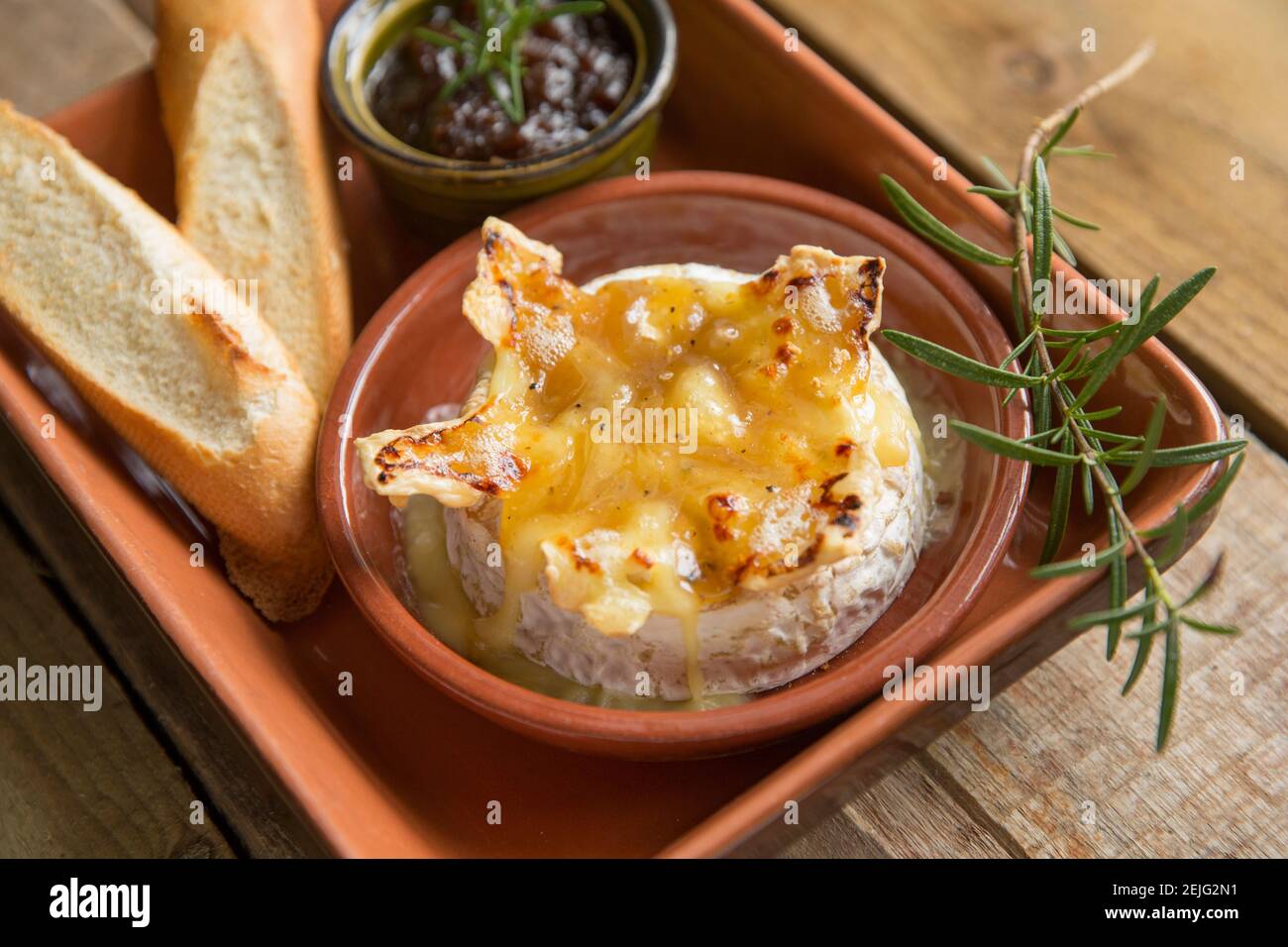 French Camembert that has been baked in an oven with a truffle, garlic and honey sauce, served with toasted French bread and caramelised onion chutney Stock Photo
