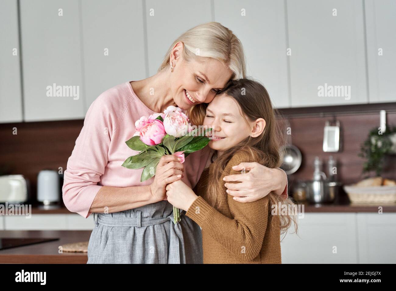 Happy mom receiving flowers from teen child daughter on Mothers Day. Stock Photo