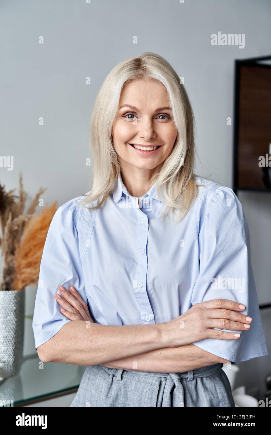 Smiling confident 50s middle aged woman standing arms crossed at home office. Stock Photo