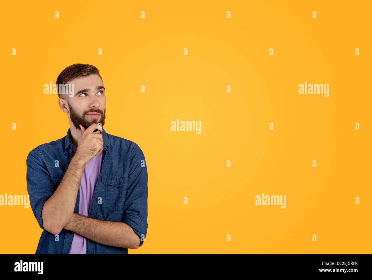 Dreamy hipster guy thinking over something, looking at empty space on orange studio background Stock Photo