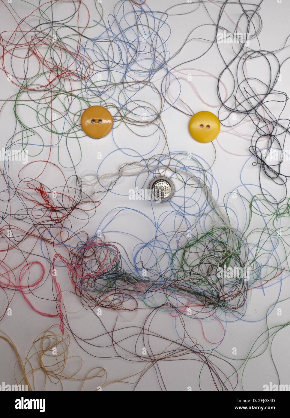 Tangle of sewing thread in various colors in the shape of a white