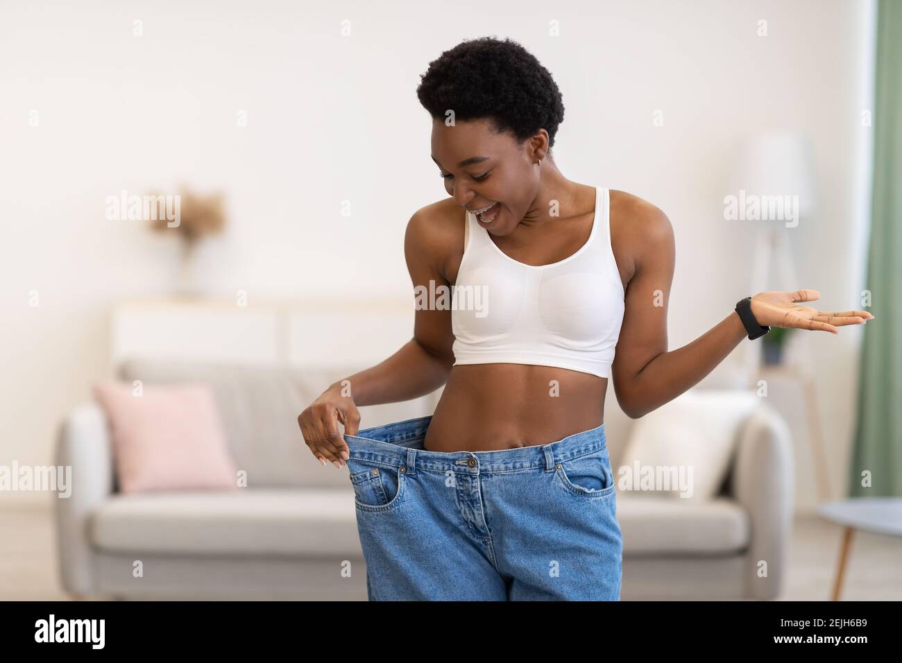 Excited Slim African Woman Wearing Oversized Pants After Weight-Loss Indoor Stock Photo