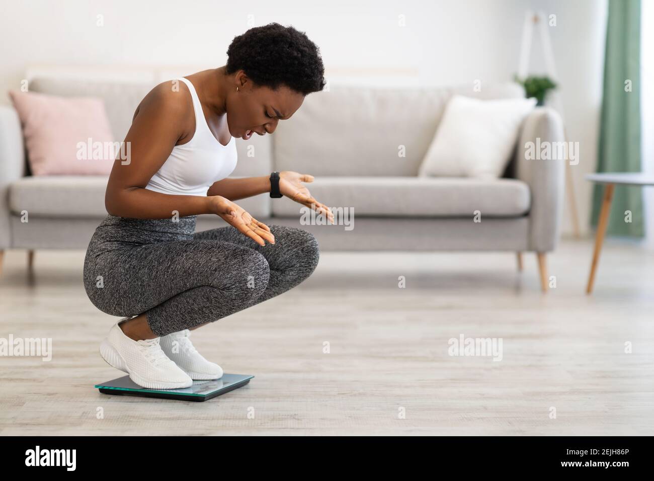 Frustrated Black Lady Looking At Scales After Weight Gain Indoor Stock Photo
