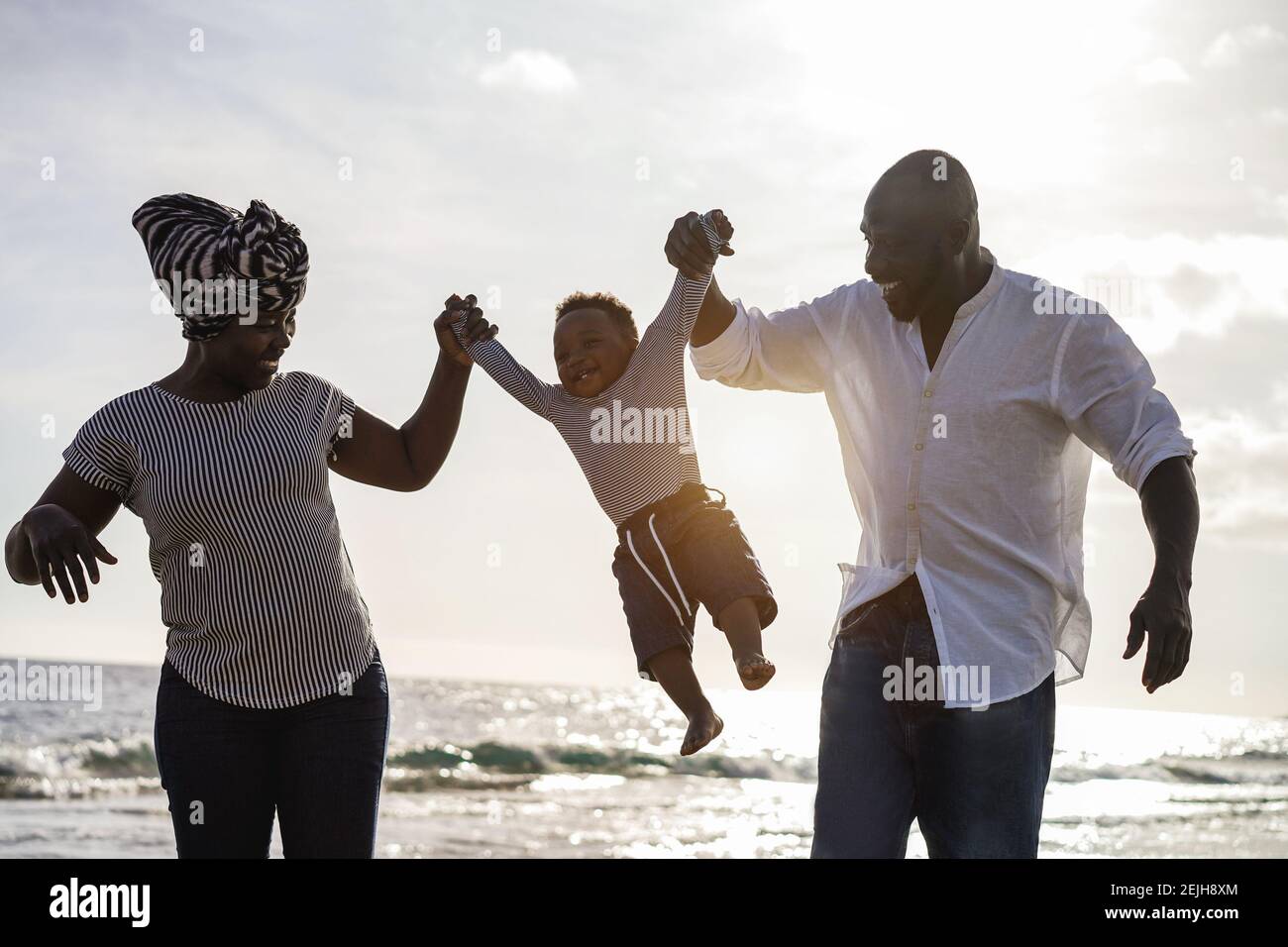 African parents and little son having fun on the beach at sunset - Family people and love concept - Main focus on kid body Stock Photo
