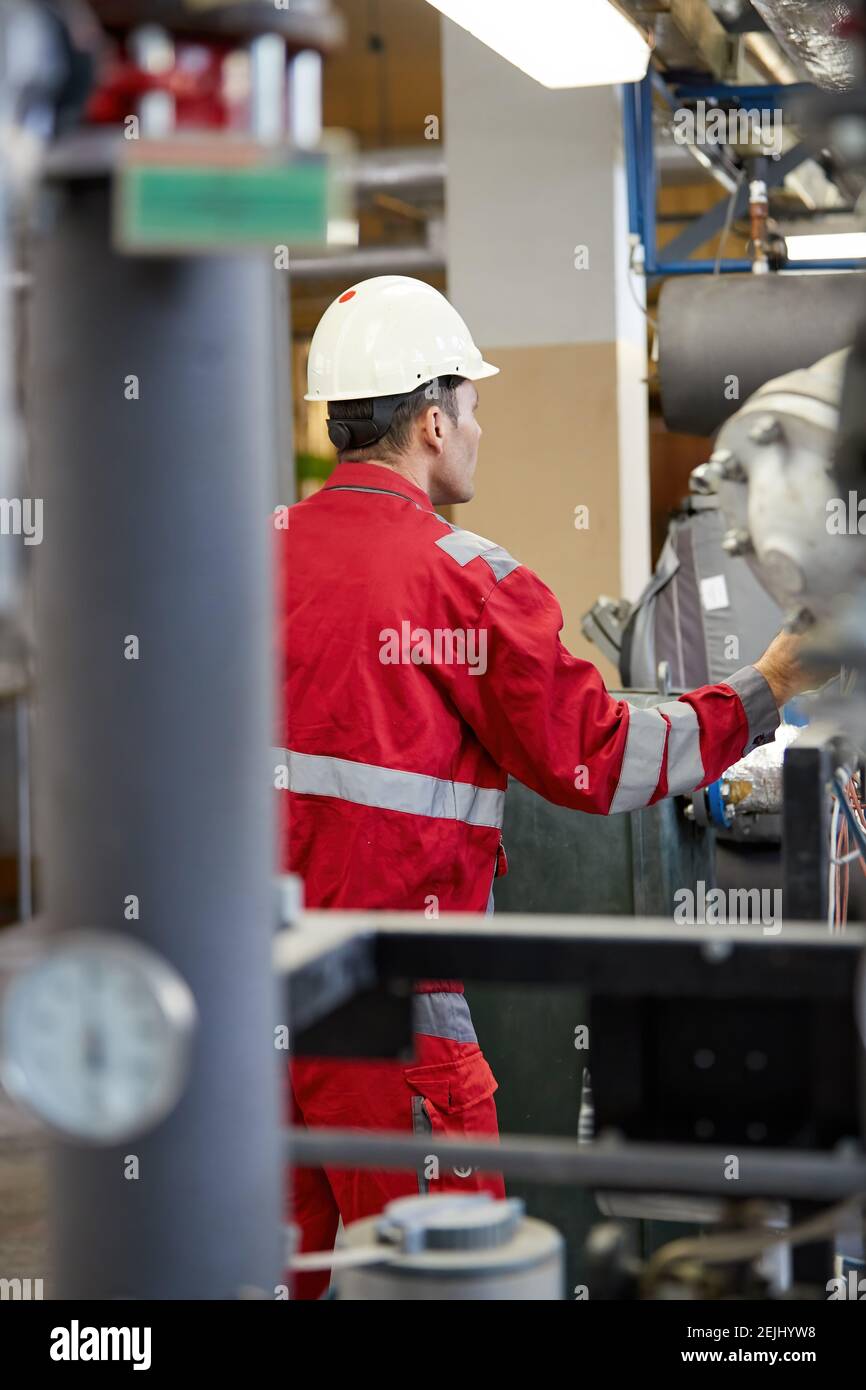 Energy industry theme: A technician in red coveralls and white helmet checks heating parameters on thermometers. Maintenance and inspection. Stock Photo