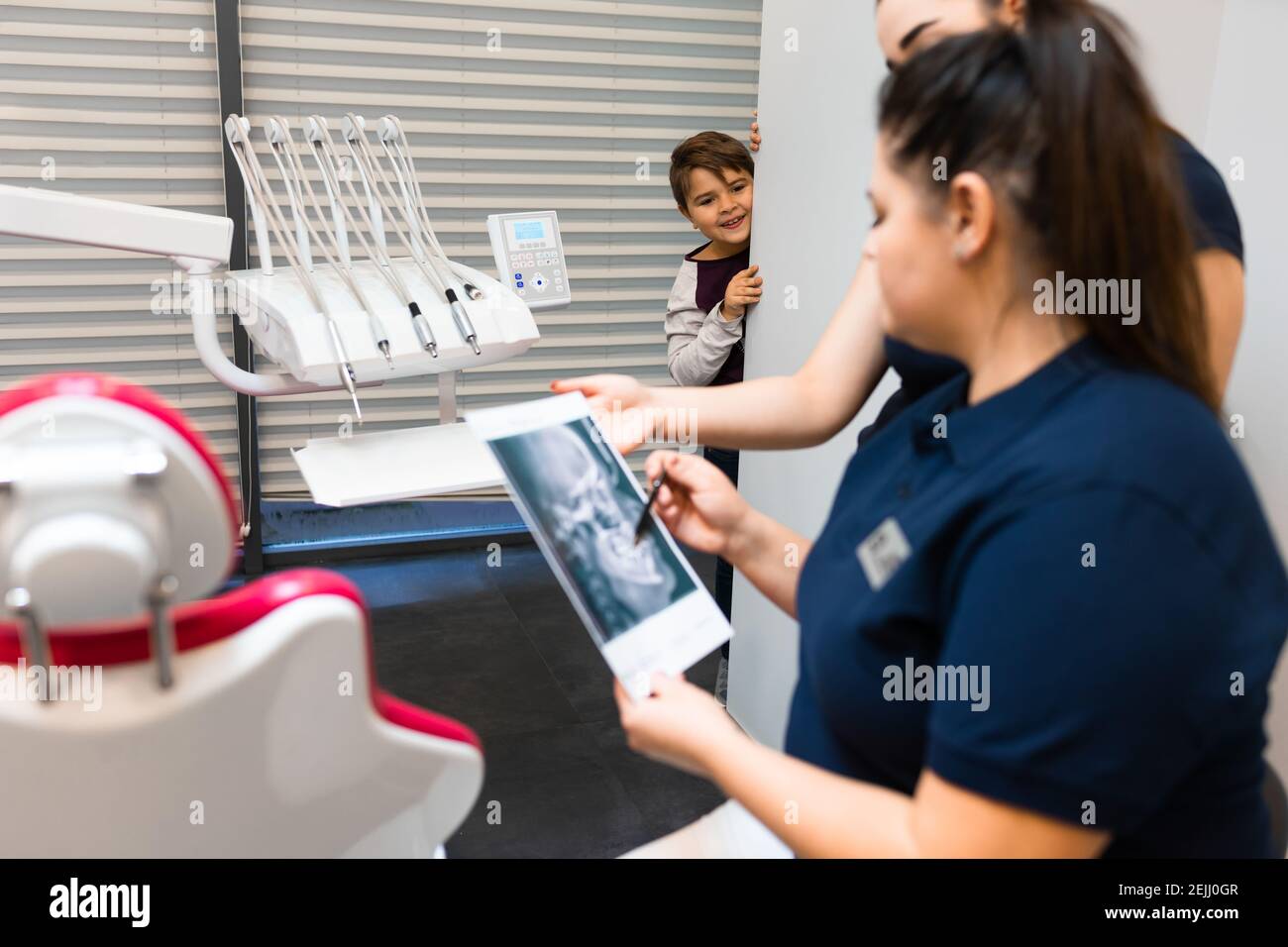 Teenager is hiding peeking out of the wall as dentists look at his x-ray. Boy still does not understand the seriousness of the health problems.  Child Stock Photo