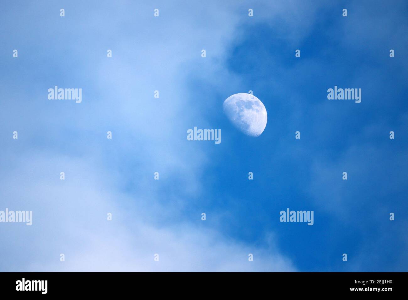 Rising moon in blue sky with white clouds Stock Photo