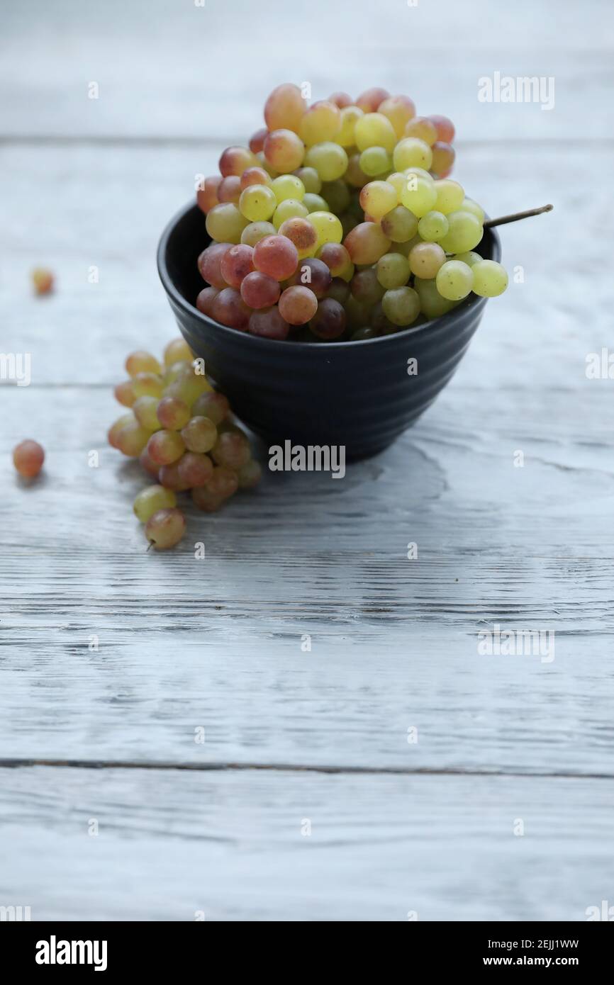 Red green grapes in a black bowl on a gray wooden table and copy space. Stock Photo