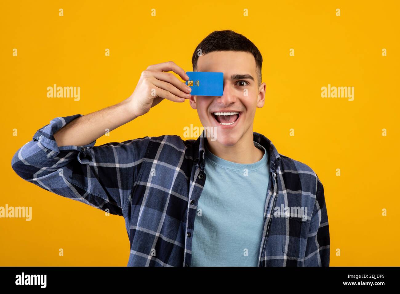 Handsome young guy covering his eye with credit card over orange studio ...