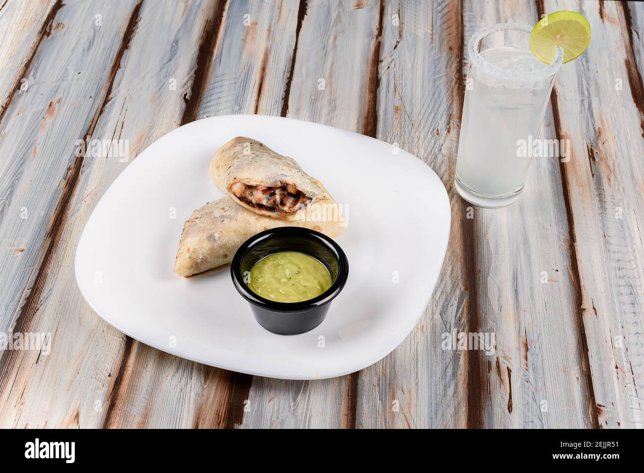 Closeup of a taco or burrito served with Mexican guacamole on a table Stock Photo