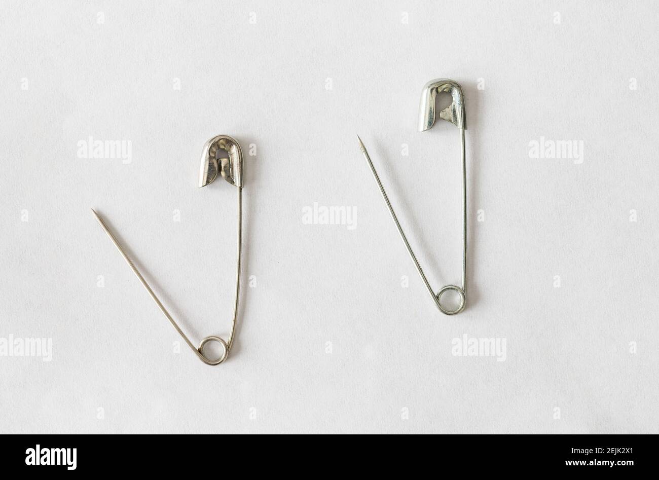 two open silver safety pins on white background Stock Photo