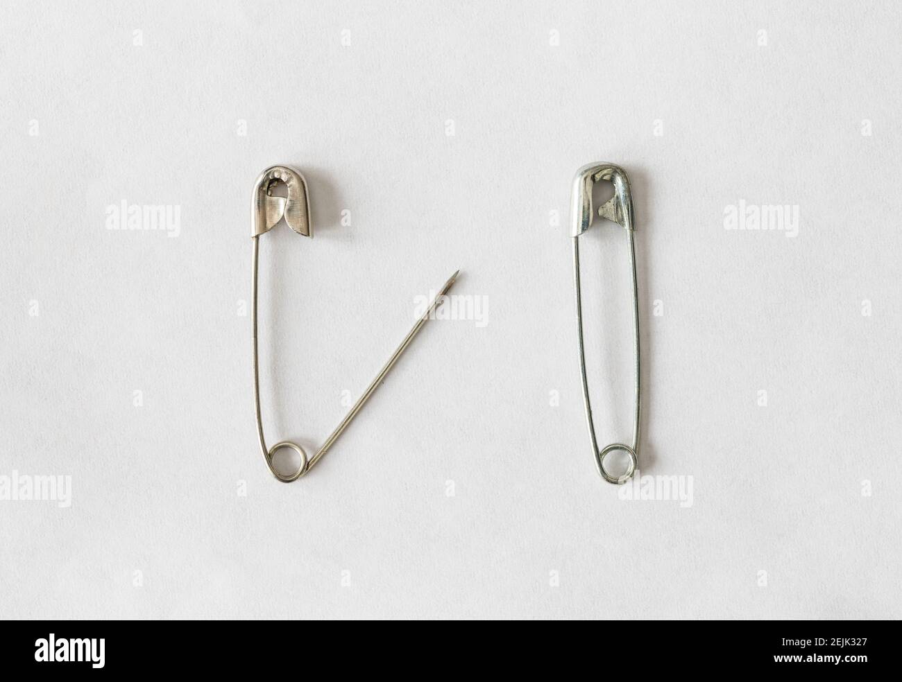 Two silver safety pins on white background, open safety pin on left, closed safety pin on right Stock Photo