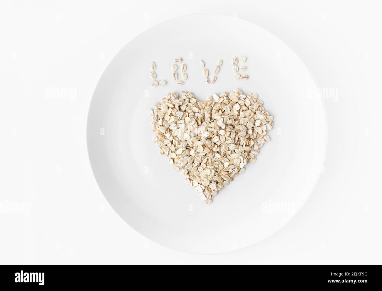 Heart of oatmeal on a white plate on a white background. Inscription Love from flakes. Space for text.  Stock Photo