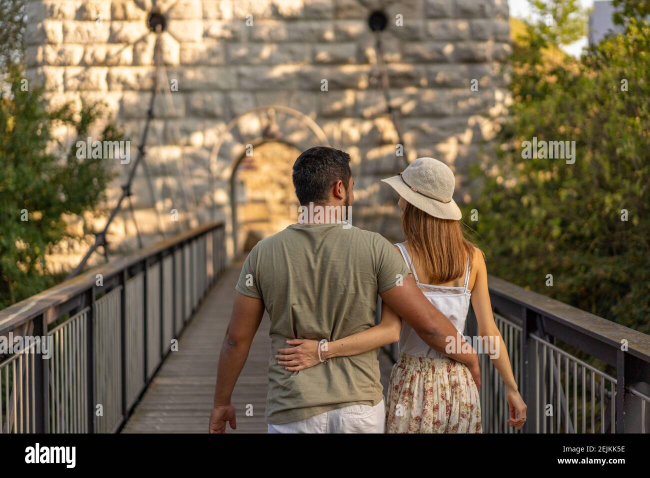 Rear view of young couple, walking embraced on wooden platform of hanging bridge of Aare river at late afternoon in September at sunset. Stock Photo