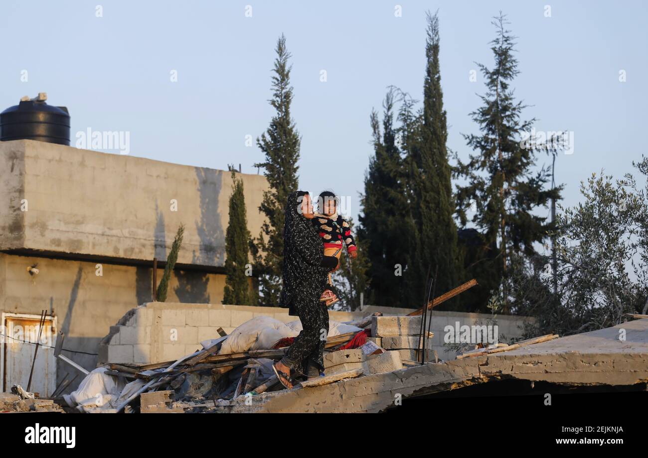 A Palestinian woman carrying her child walks next to the rubble of ...