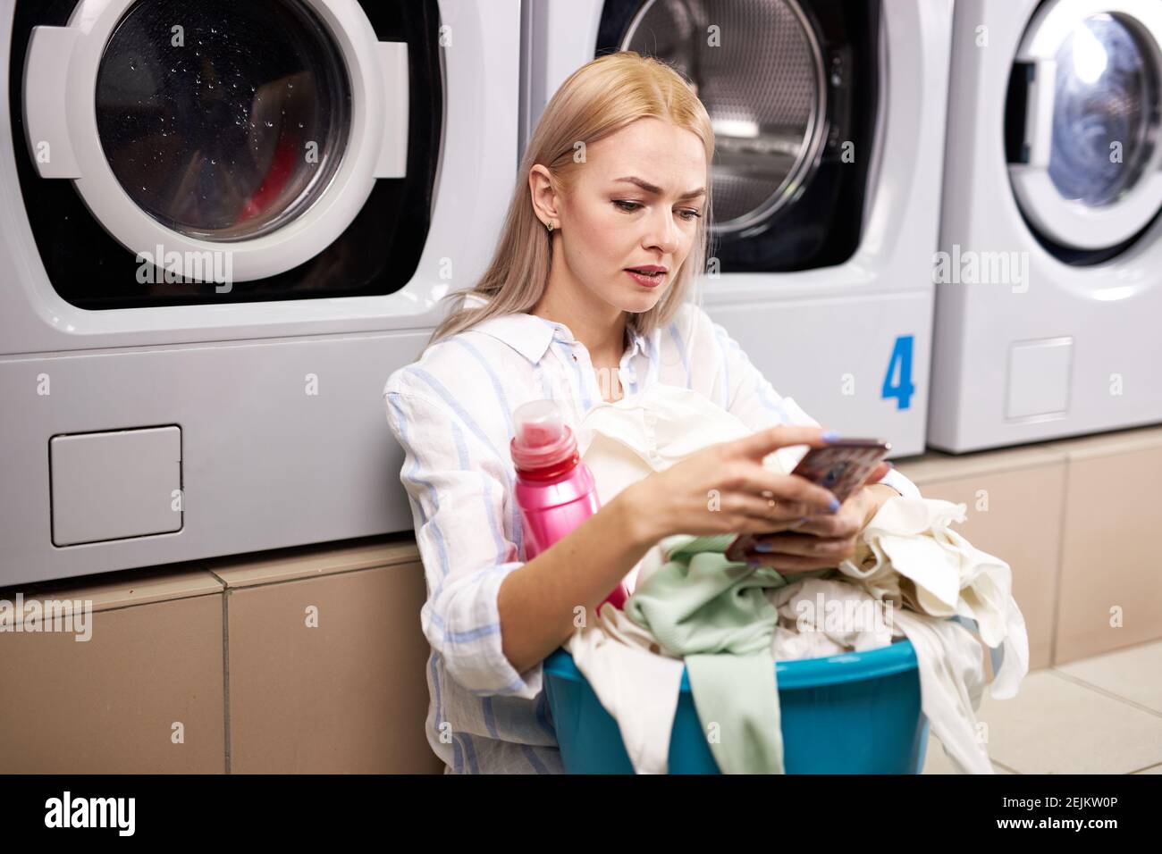 female sitting on the floor and lean to a washing machine holding a ...
