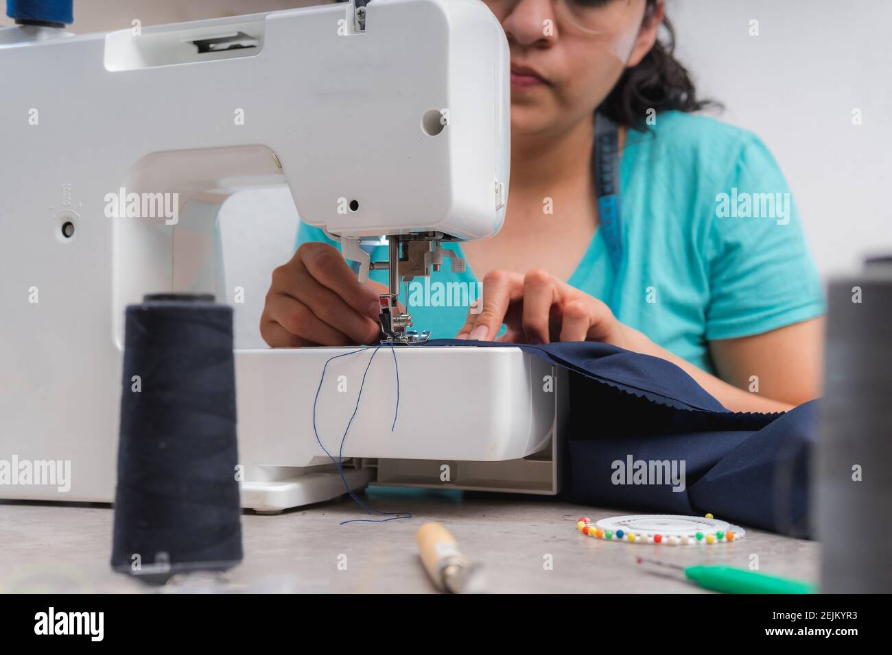 Cheerful woman sewing while sitting at her working place in fashion workshop Stock Photo