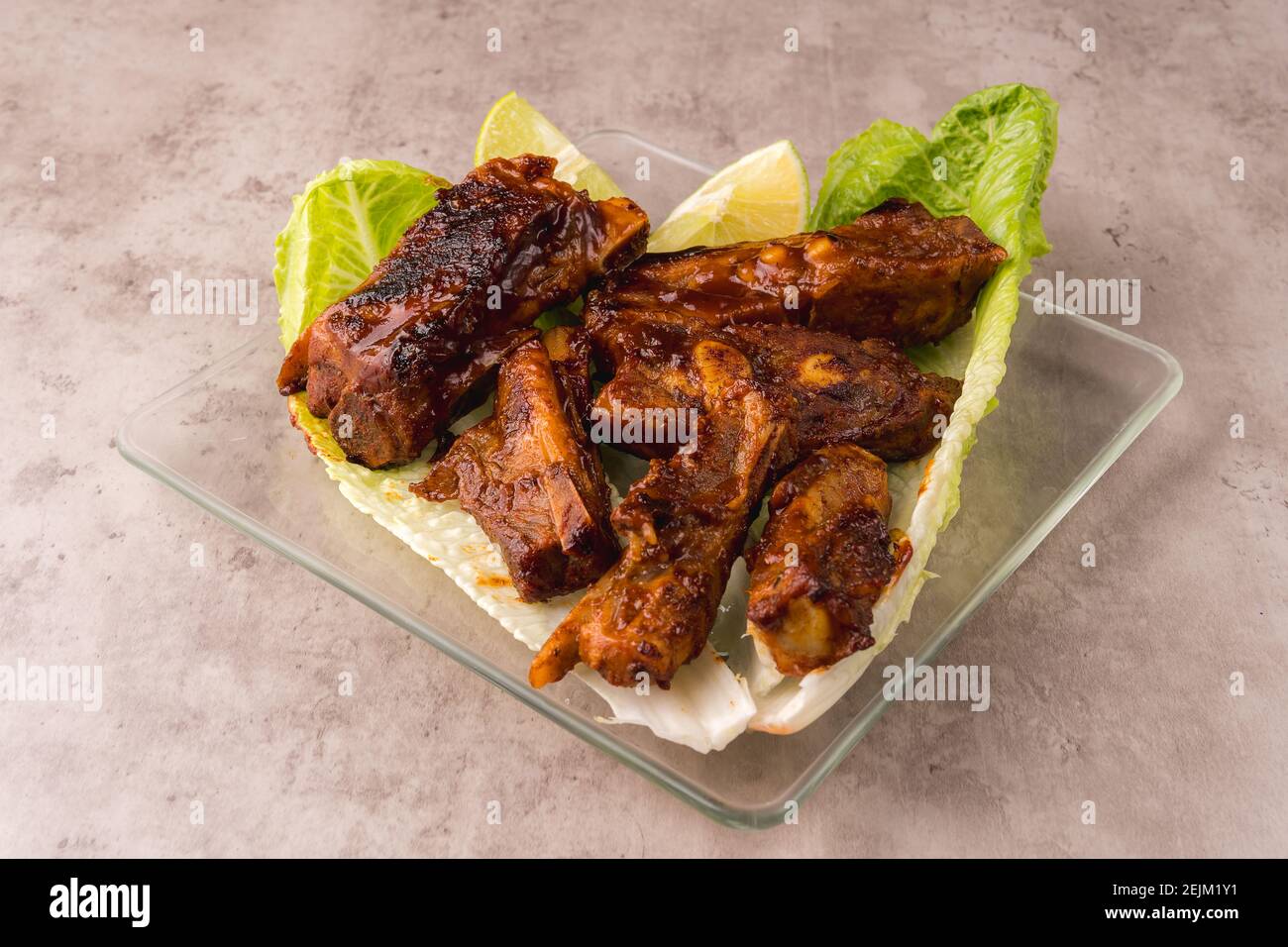 Plate of hot pork ribs prepared on the grill with BBQ sauce on a bed of fresh lettuce Stock Photo