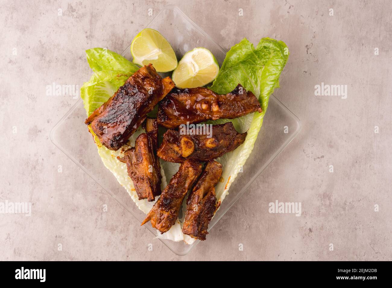 Plate of hot pork ribs prepared on the grill with BBQ sauce on a bed of fresh lettuce Stock Photo