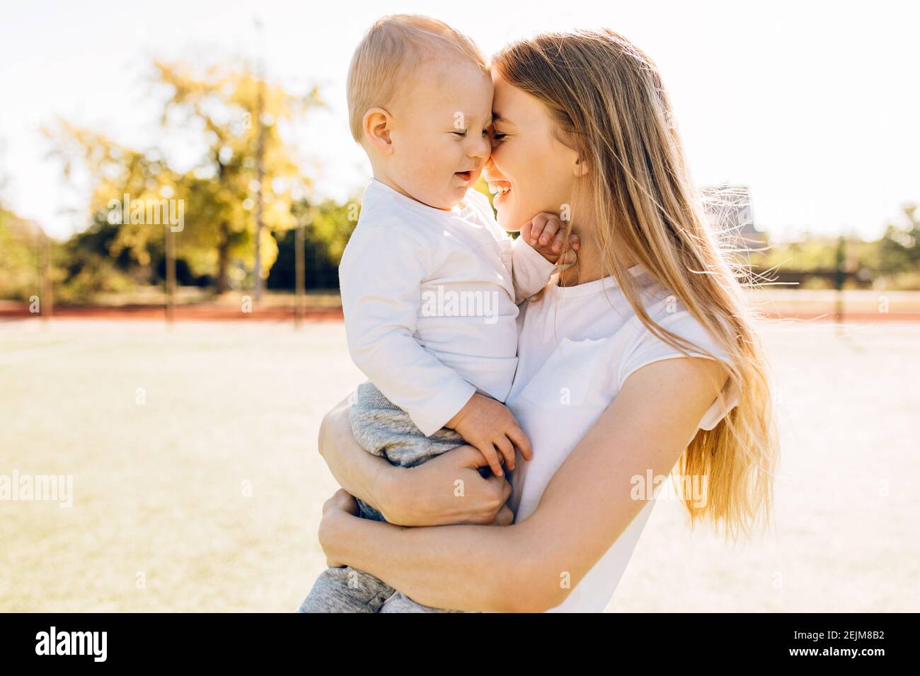 Caring young mother with her baby, loving mom hugs little child, enjoying tender family moment outdoors on a sunny day, Mother's Day Stock Photo