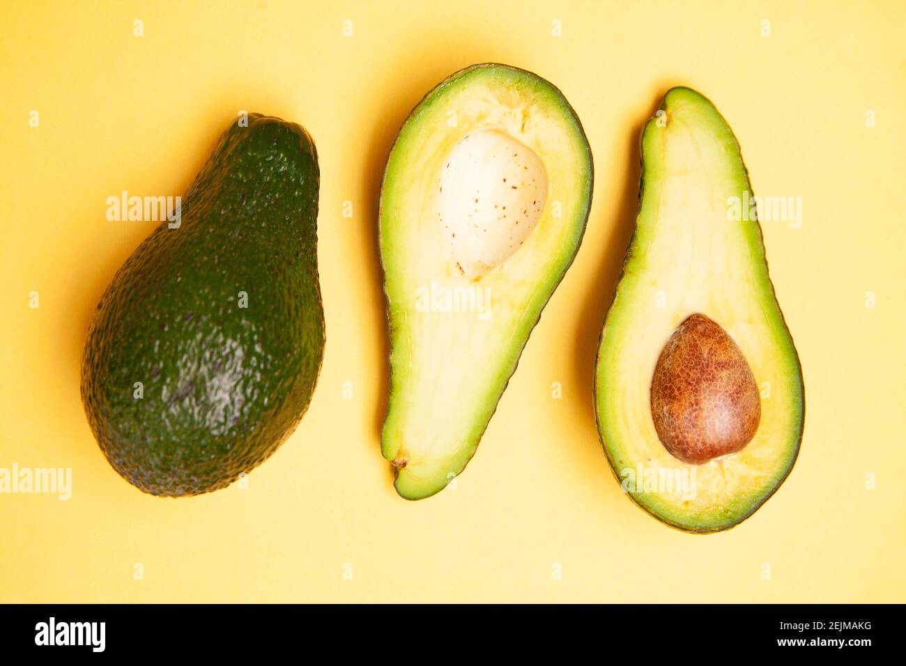 Halved and whole avocados on yellow table Stock Photo - Alamy