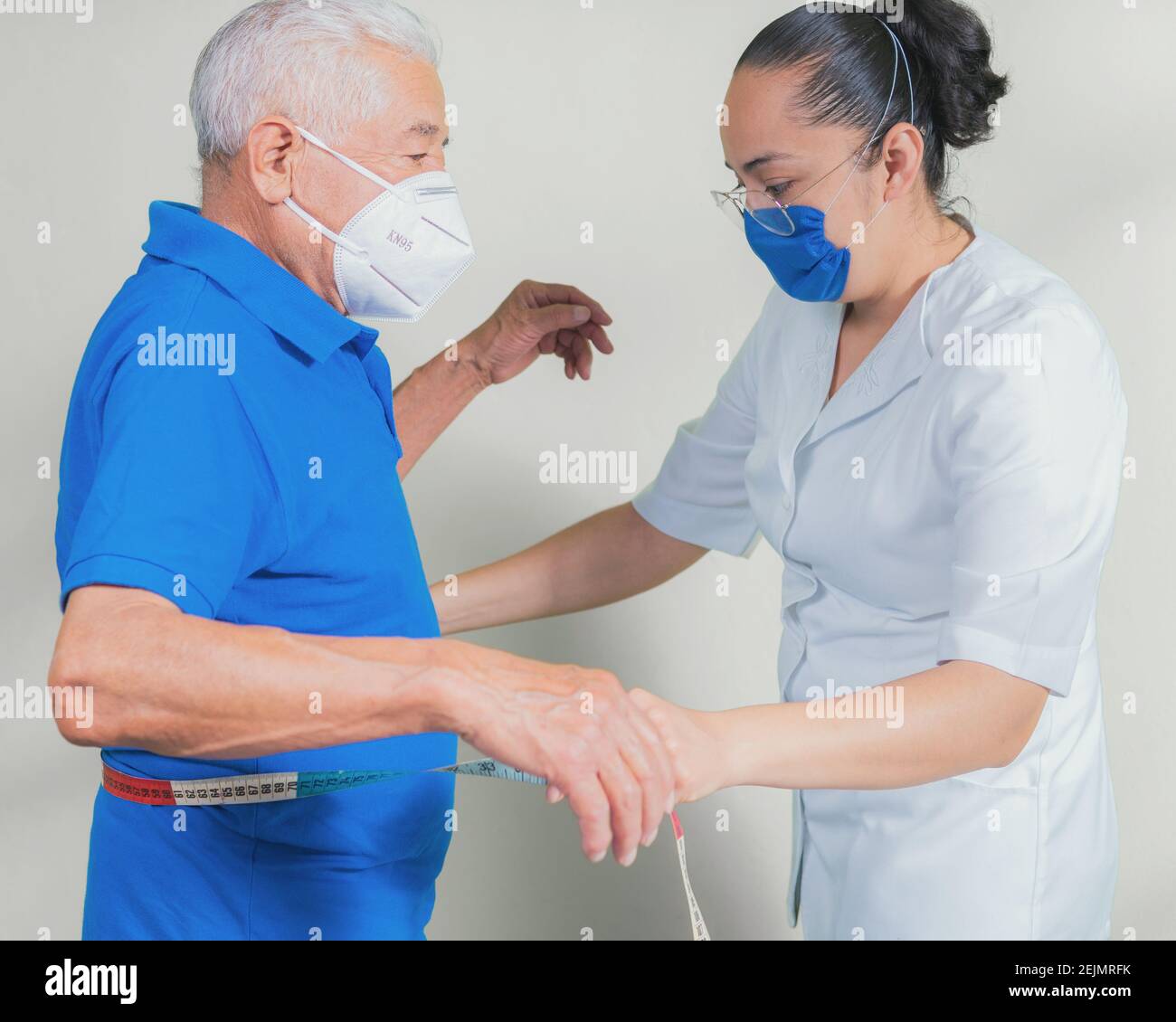 View of a nurse passing the tape measure on the height of an older man to measure his obesity Stock Photo