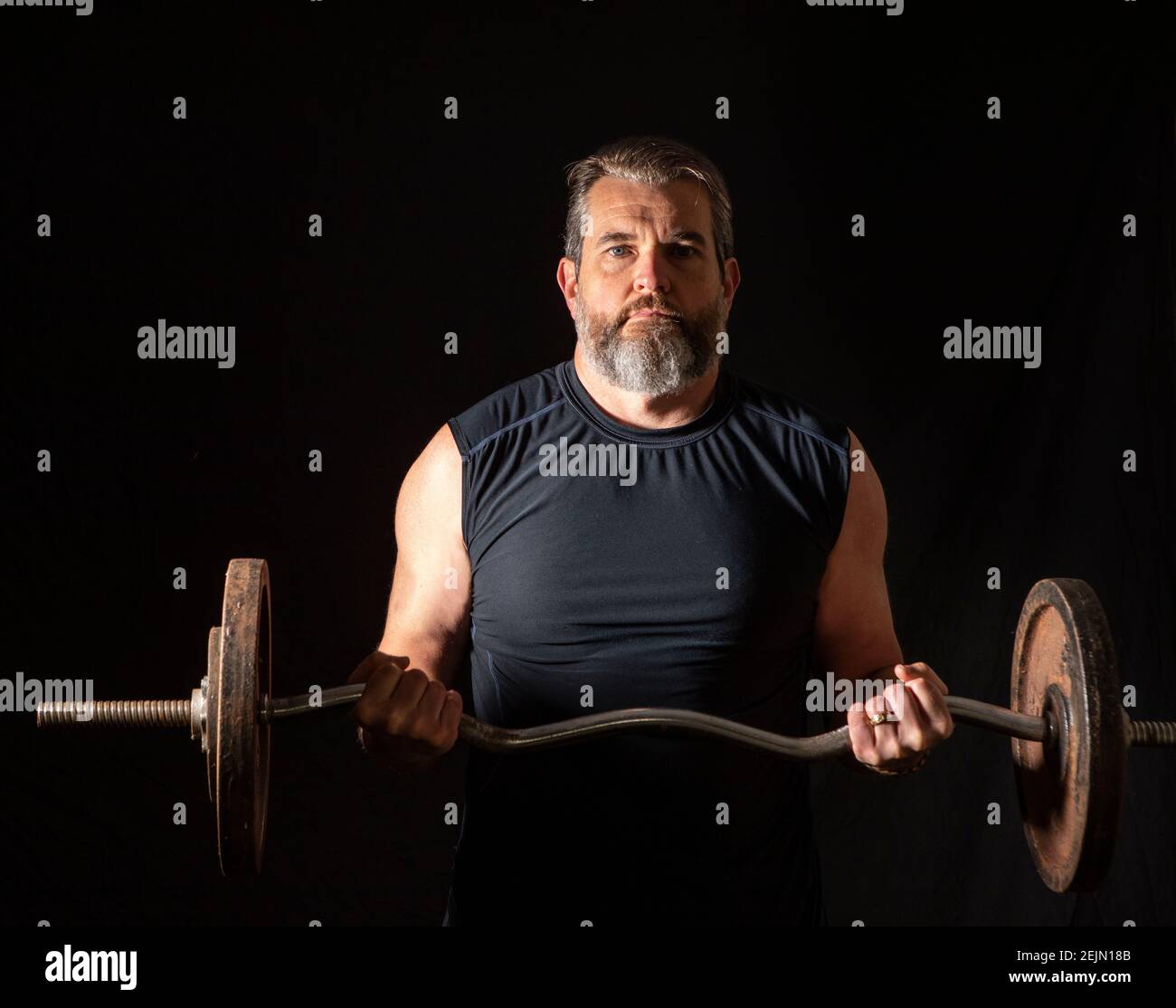Strong, active, middle aged man with gray beard lifting heavy weights in studio setting. Stock Photo