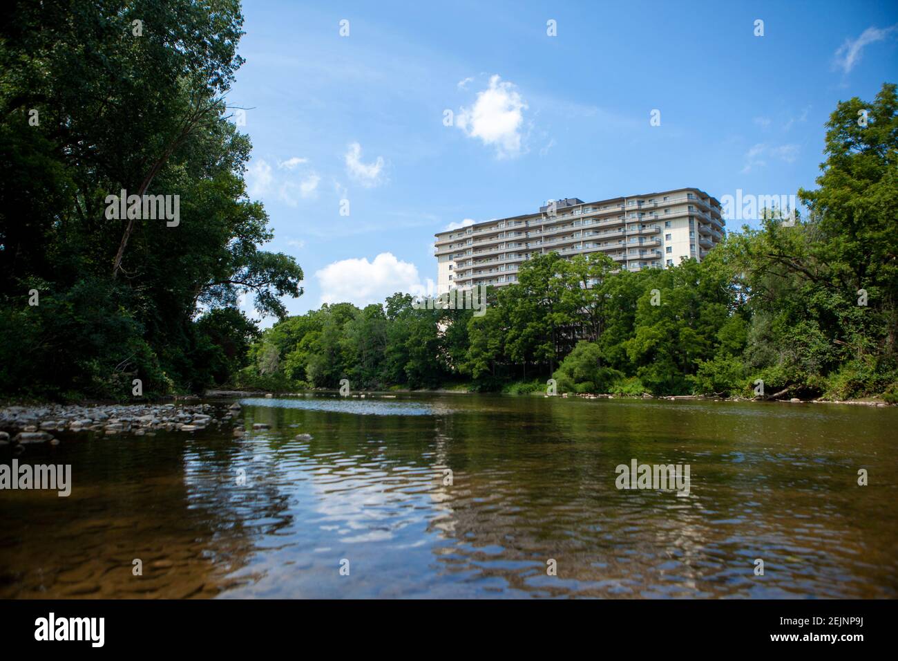 Apartment Building on the Thames River under Blue Summer Sky in London Ontario Canada with clear fresh water and surrounded by forest trees on the sho Stock Photo
