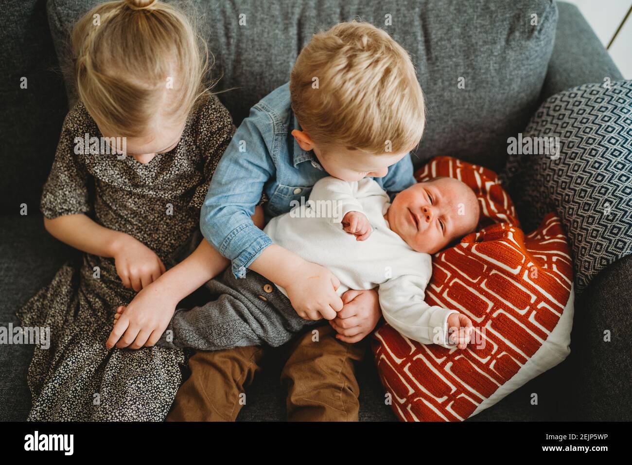 Baby on couch at home with brother and sister holding him Stock Photo Alamy