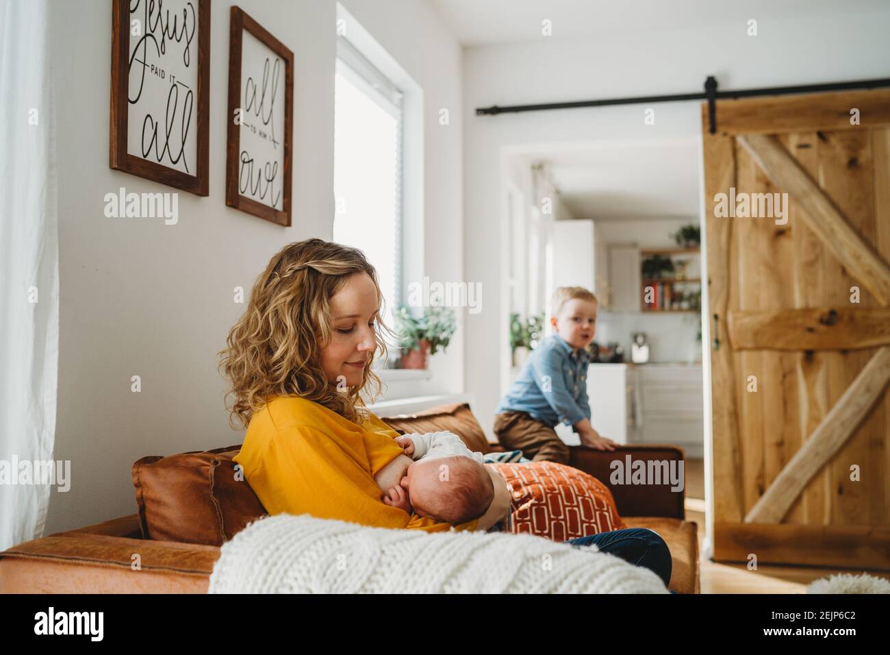 Mother breastfeeding newborn baby at home in family room with son Stock Photo